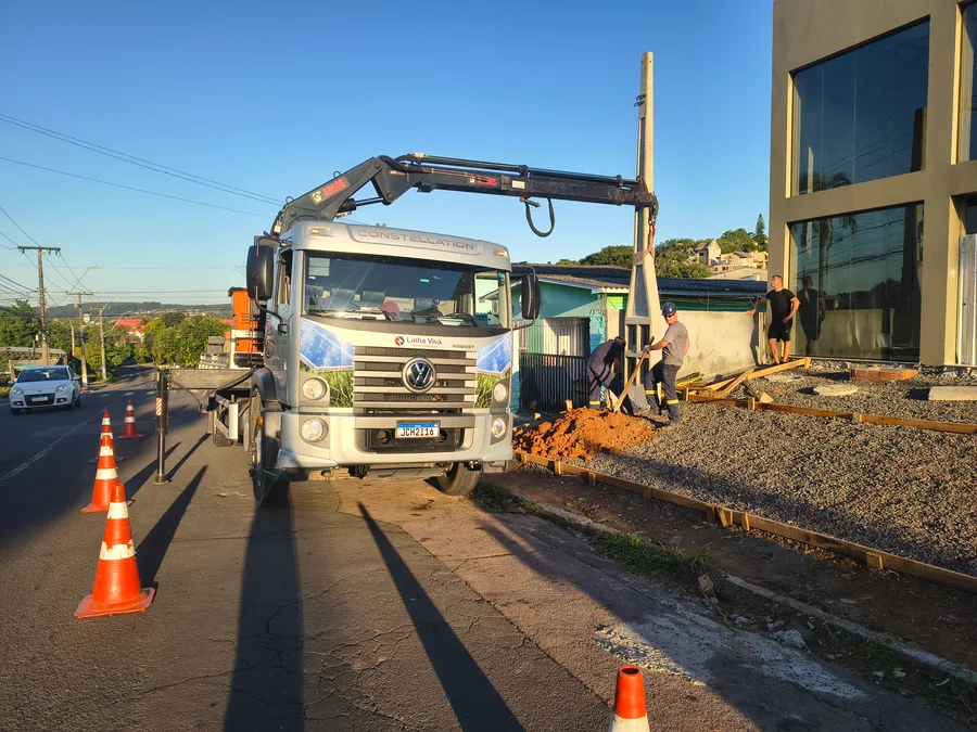 Equipe instalando poste de concreto com auxílio do caminhão guindaste